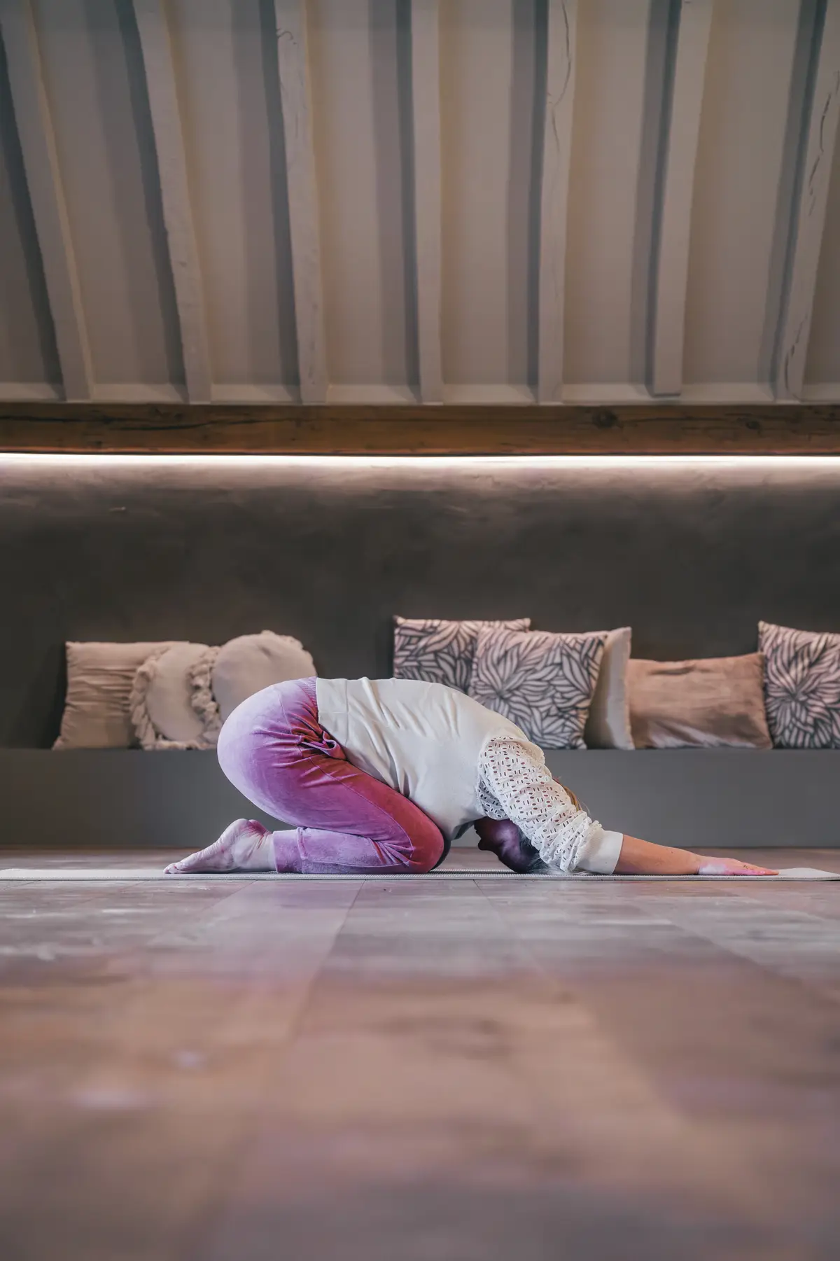 Vrouw in roze yogalegging doet child's pose in een yogastudio met lounge-kussens