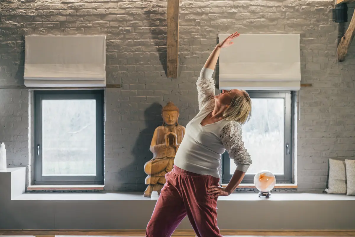Vrouw doet zijwaartse stretch in yogastudio met witte muur en houten Boeddha-beeld