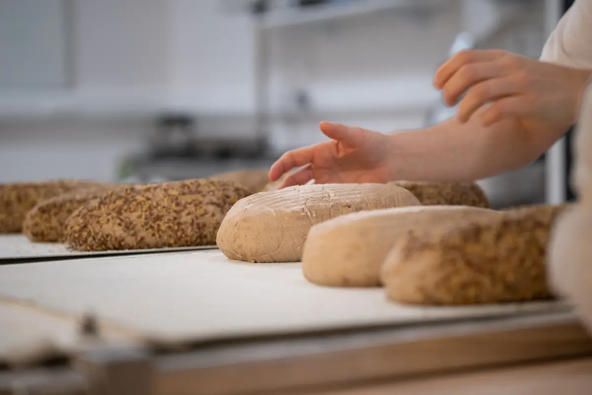 Bakker vormt verse broden op een werkbank bij Kontoer — ambachtelijk bakkerswerk